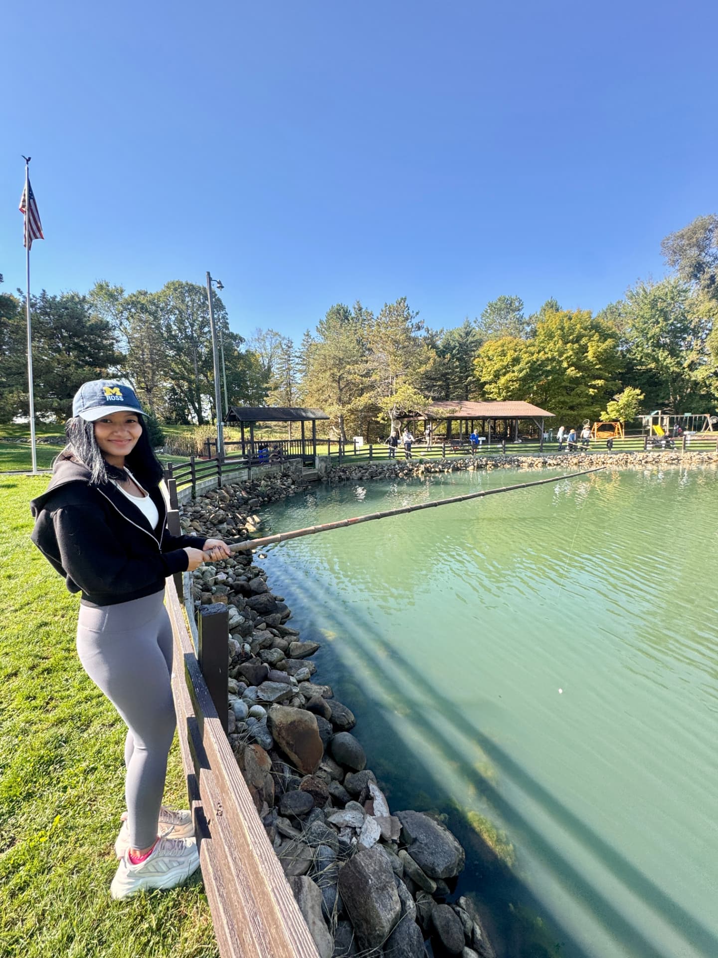 Rachel fishing at a park lake, wearing a Michigan Ross cap