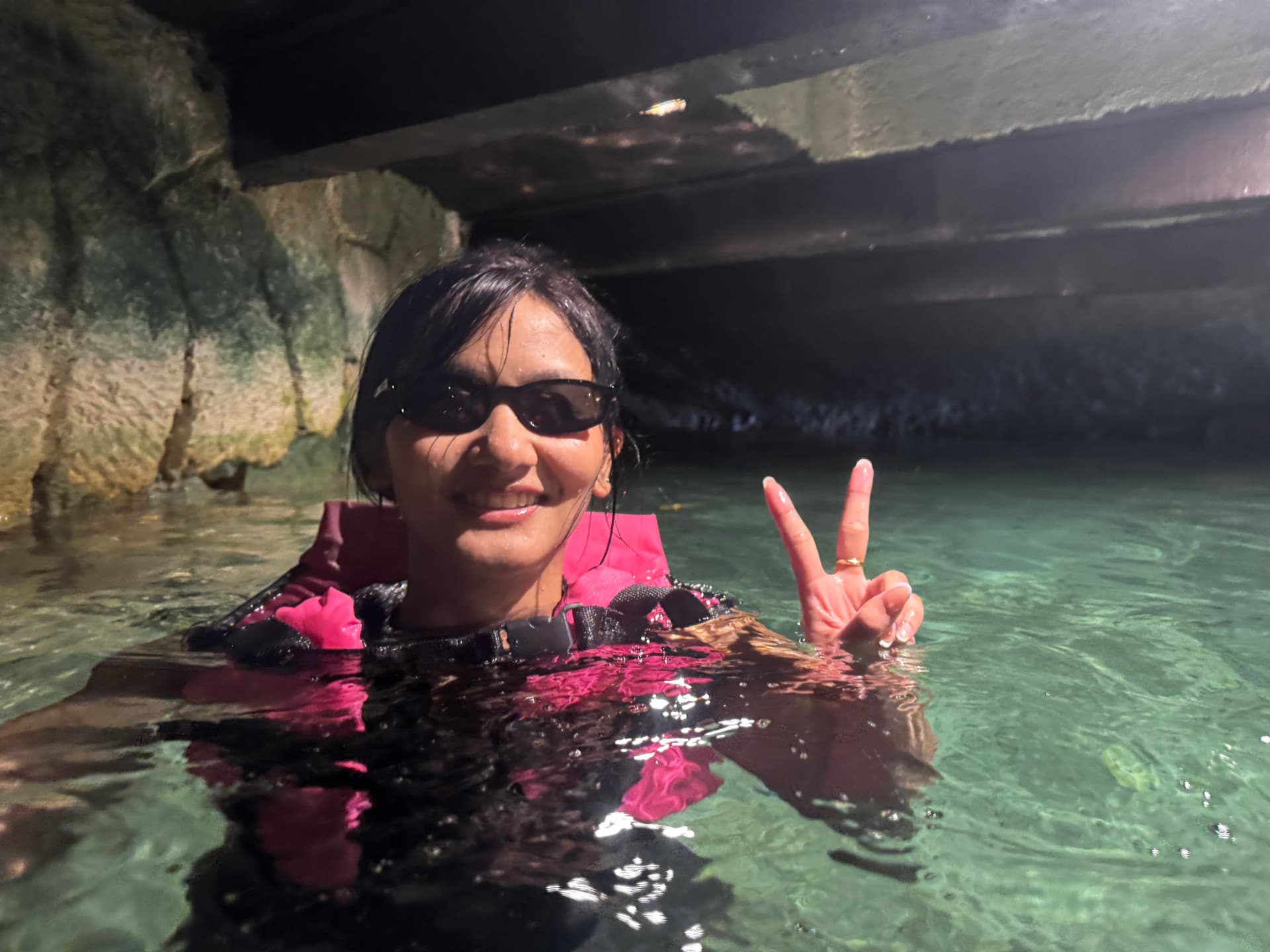 Rachel wearing sunglasses and a pink life jacket in clear water beside rock walls